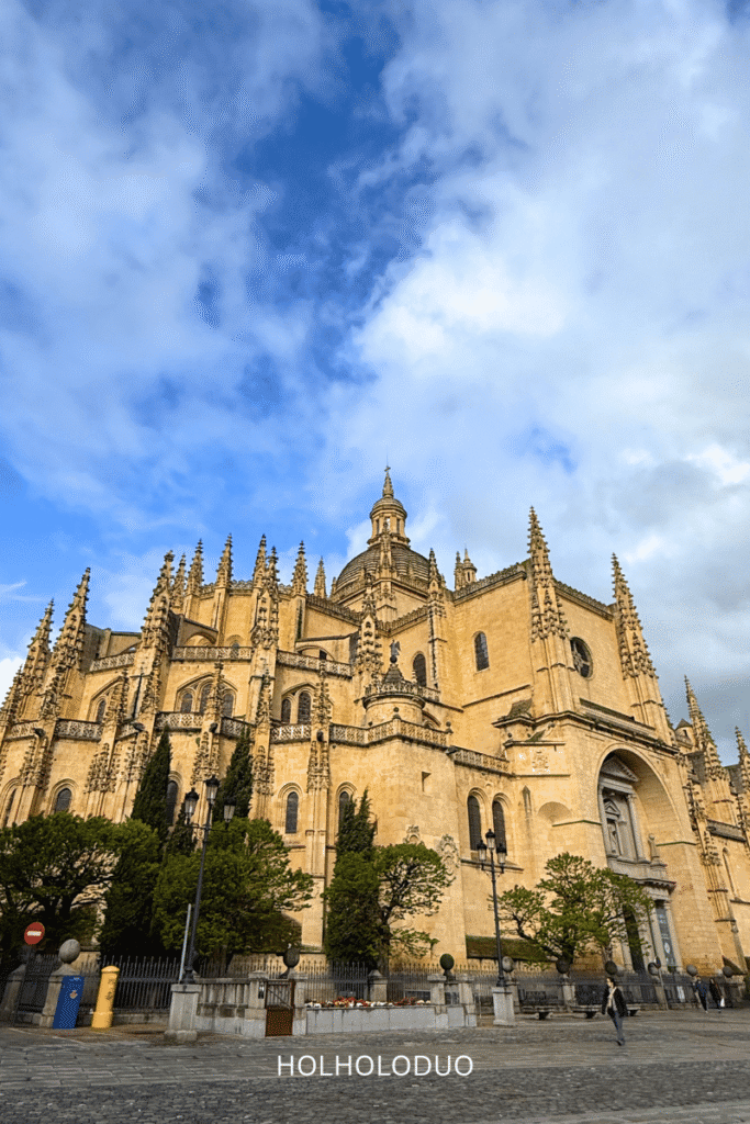 View of the Cathedral of Segovia, showcasing its intricate Gothic architecture and towering spires against a blue sky.